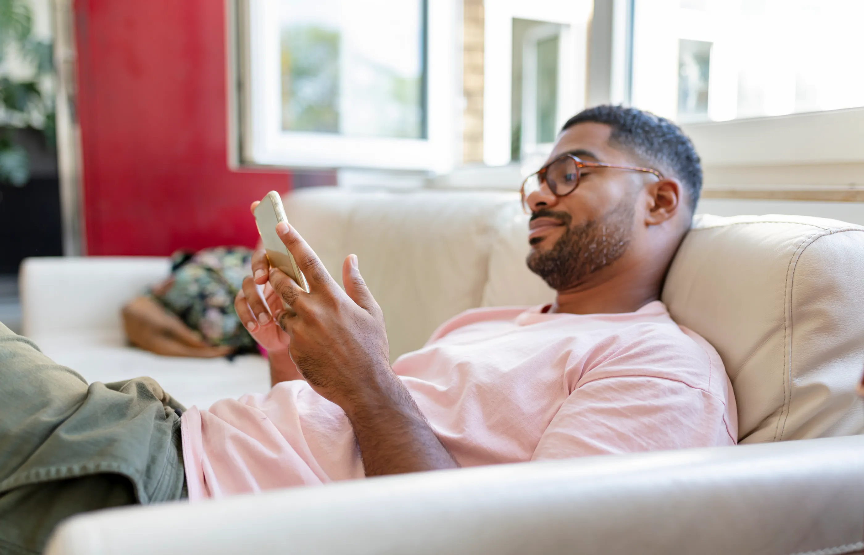 A man is lying on his couch reviewing information on his smart phone. 